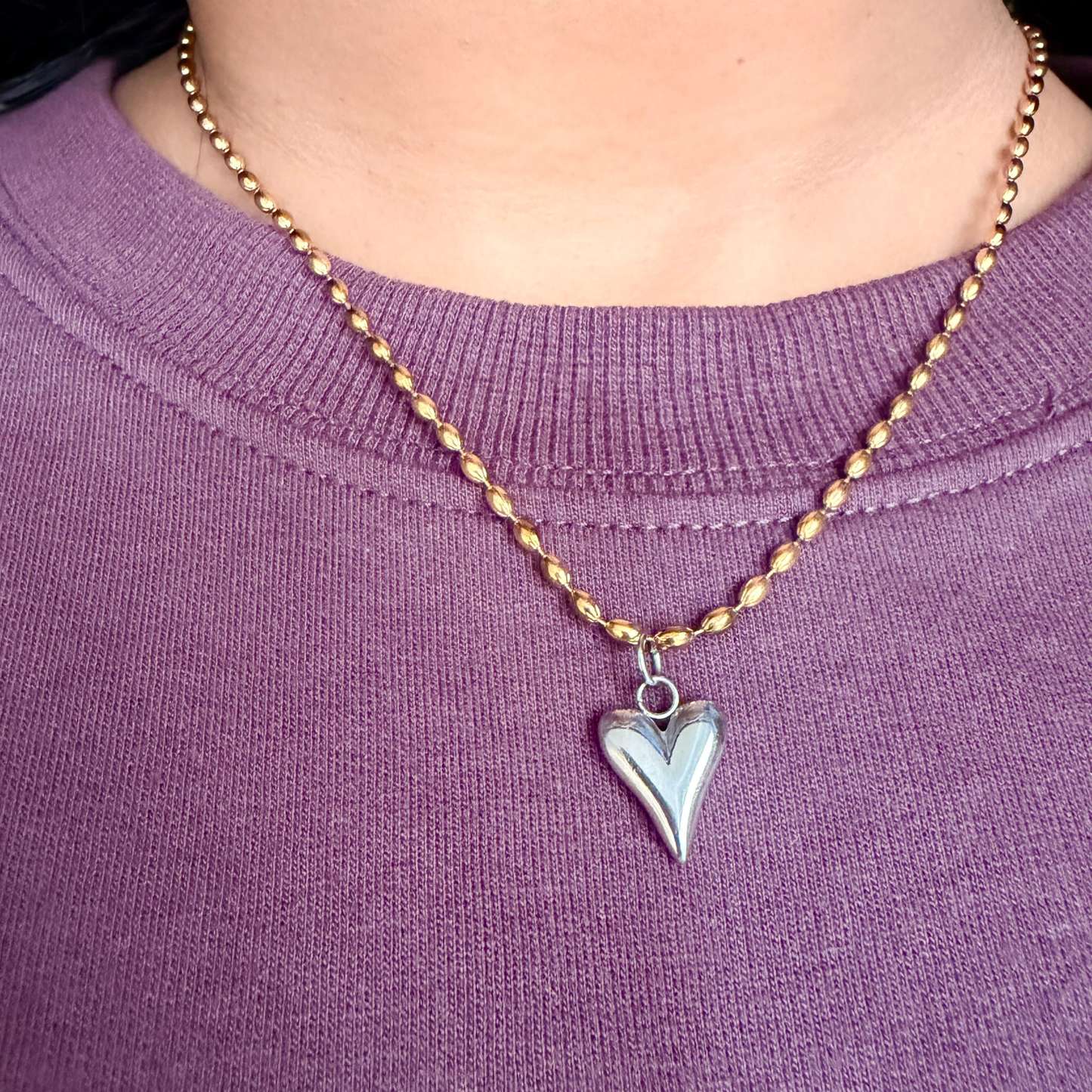Necklace with a heart-shaped pendant on a person wearing a purple shirt.