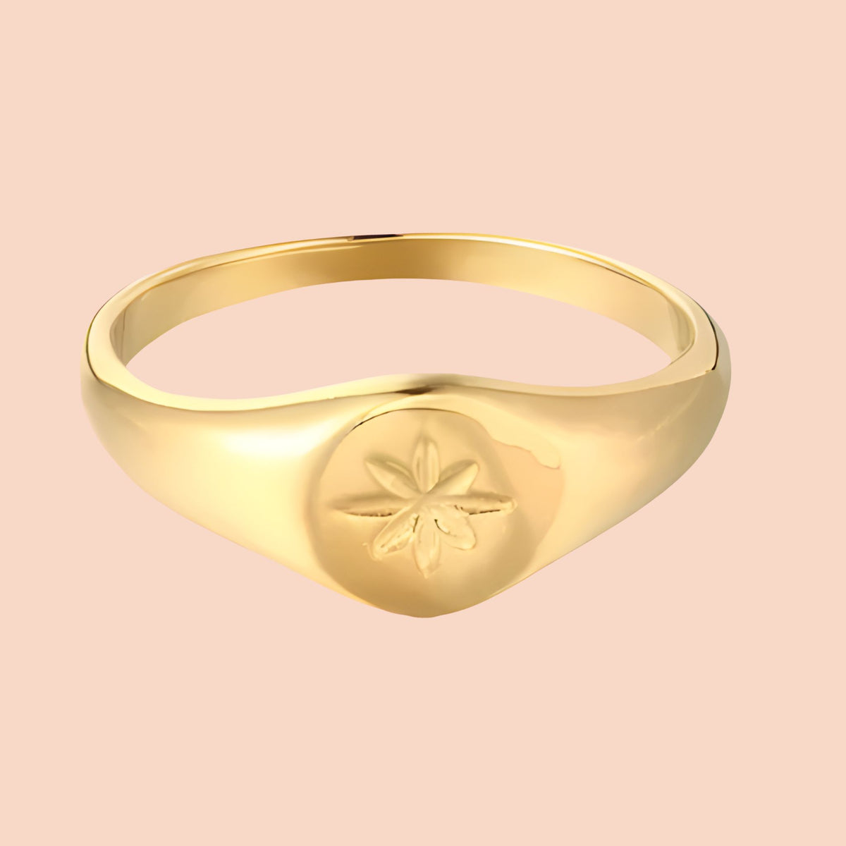 Gold ring with a star design on a pink background