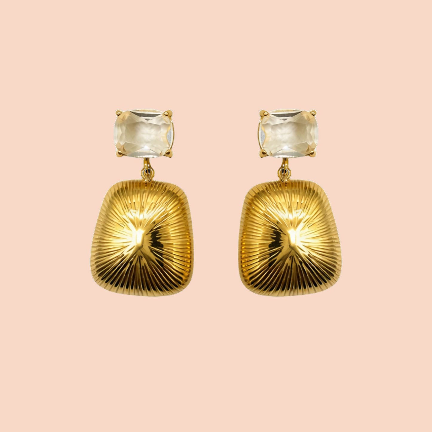 Gold earrings with clear gemstones on a pink background