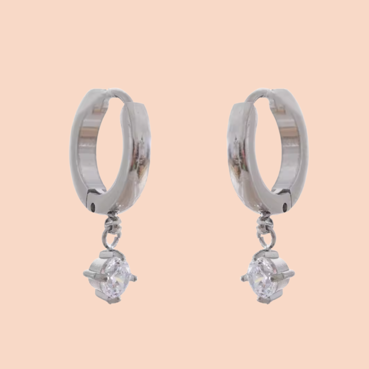 Silver hoop earrings with small diamond-like stones on a peach background