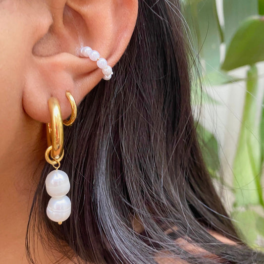 Gold hoop earring with pearl drops worn by a person with dark hair.