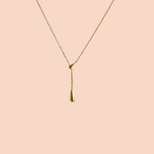 Gold necklace with a teardrop pendant on a pink background