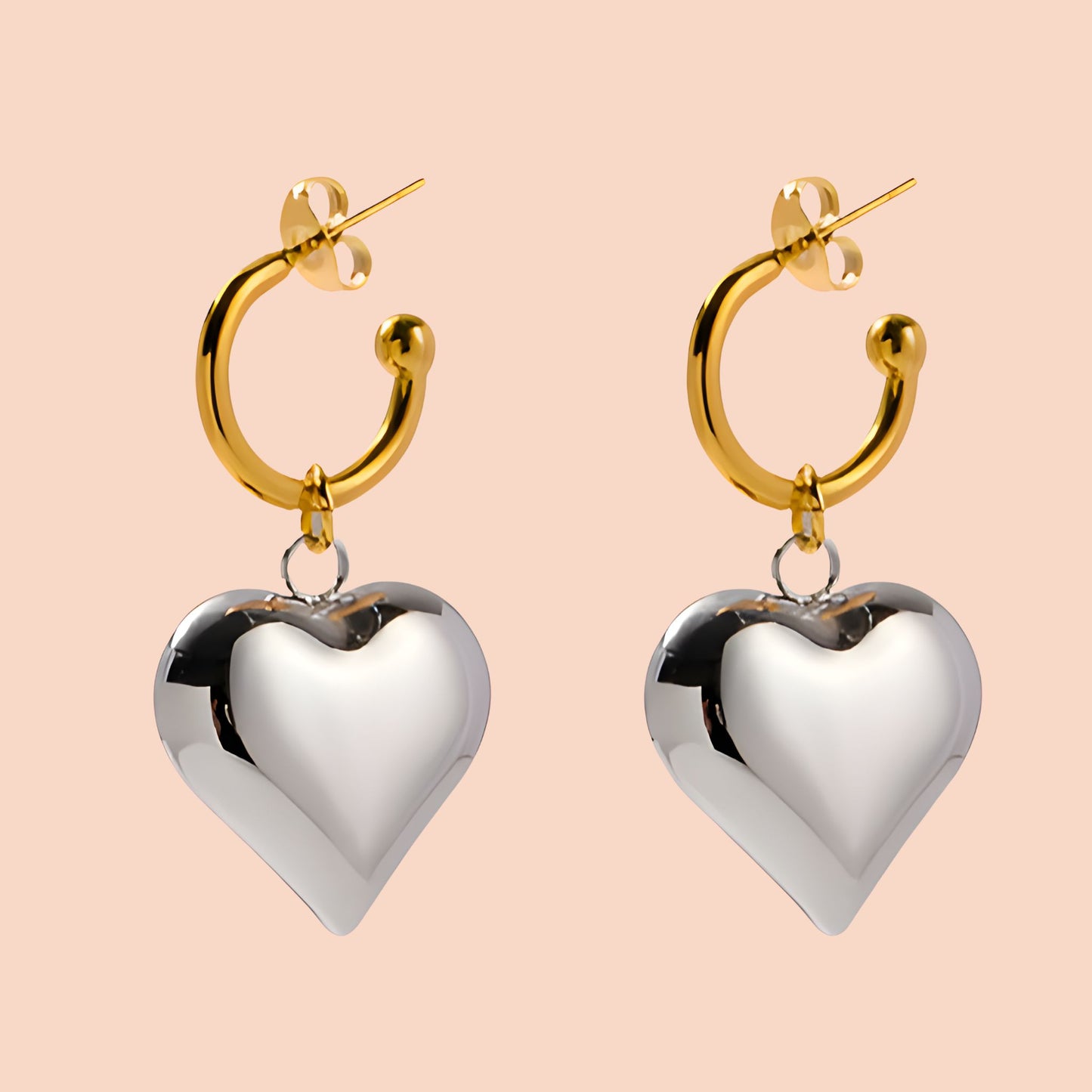 Gold hoop earrings with silver heart pendants on a beige background
