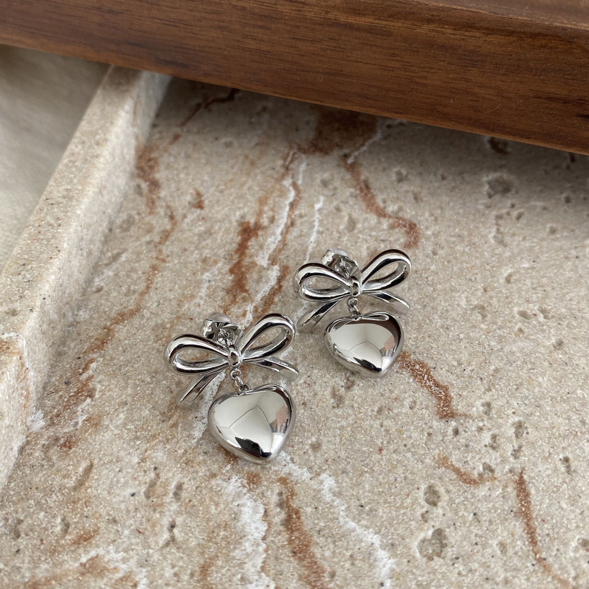 Silver bow-shaped earrings on a textured stone surface