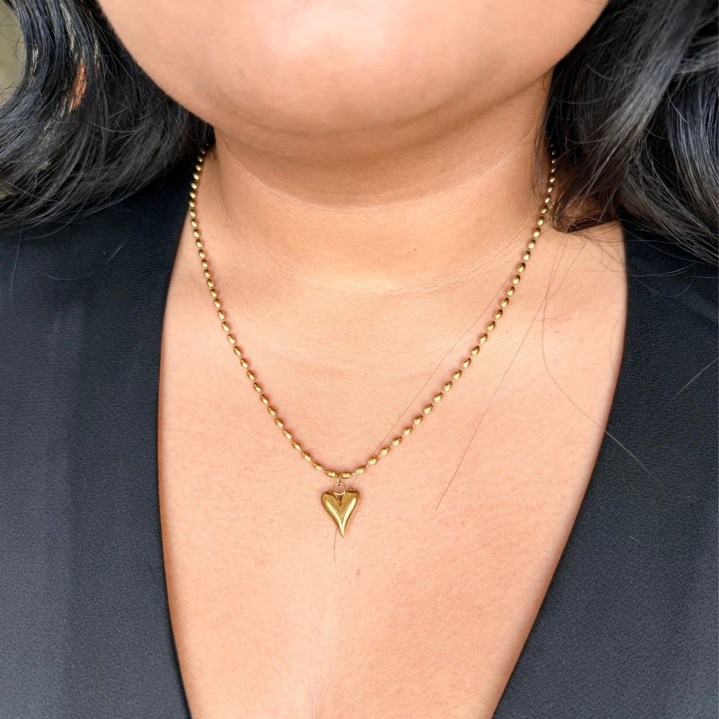 Gold necklace with a heart-shaped pendant worn by a person against a dark background