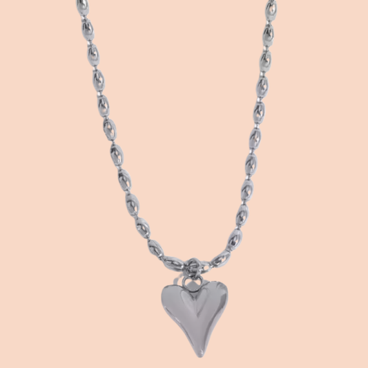 Silver heart-shaped pendant on a chain against a beige background