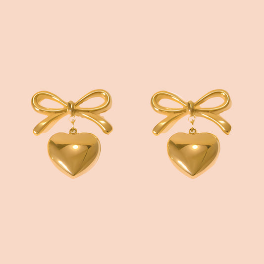 Gold bow and heart earrings on a pink background
