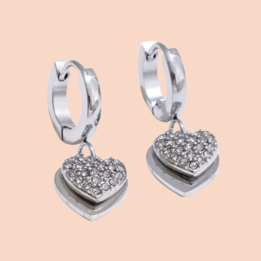 Silver heart-shaped earrings with embedded stones on a beige background