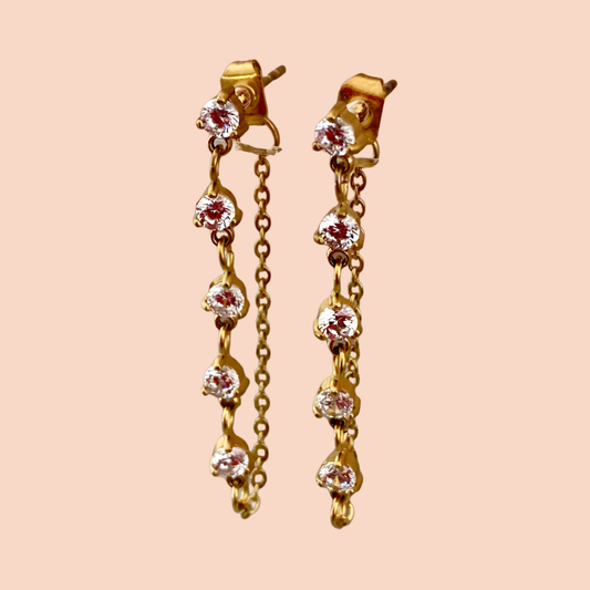 Gold earrings with gemstones on a peach background