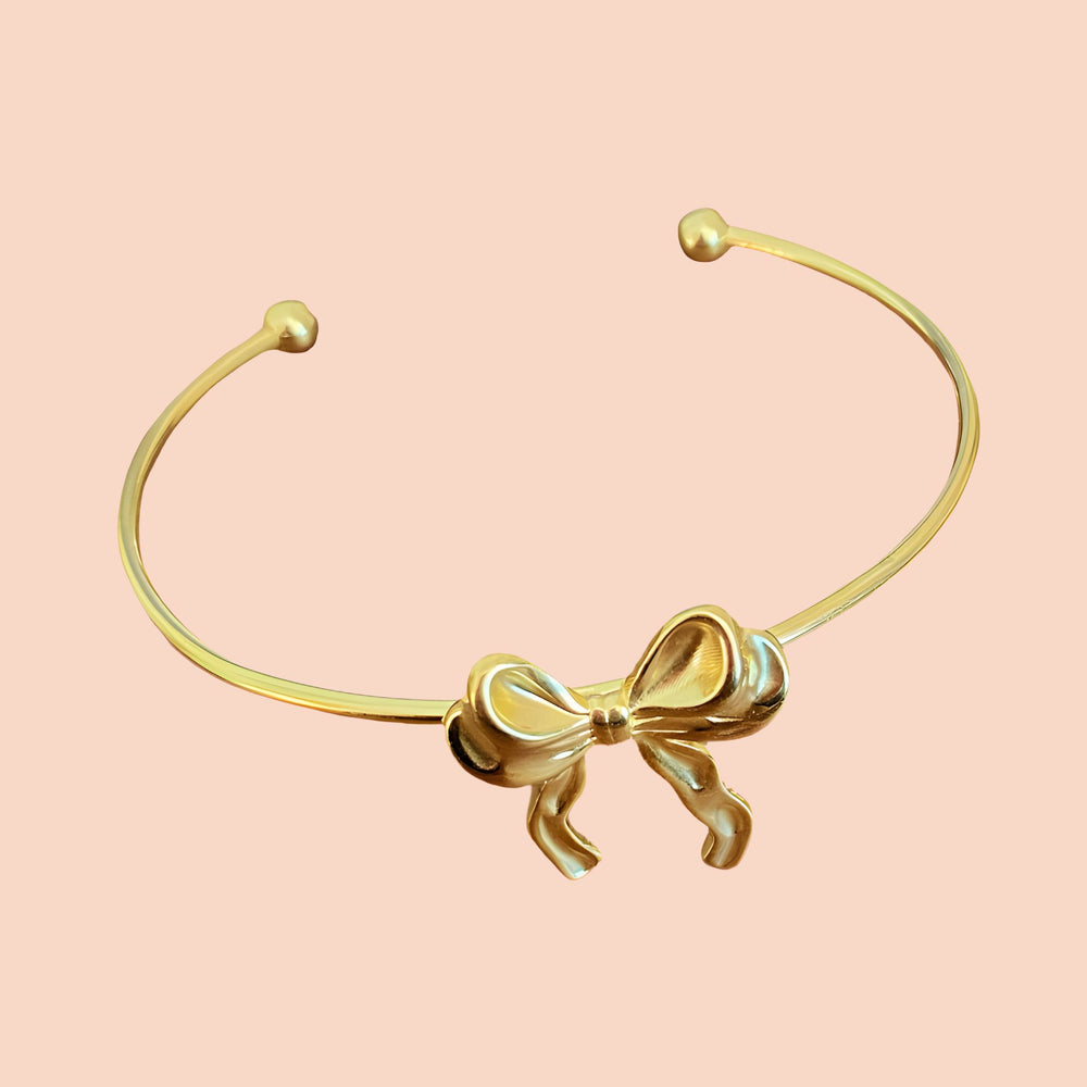 Gold bracelet with a bow design on a pink background