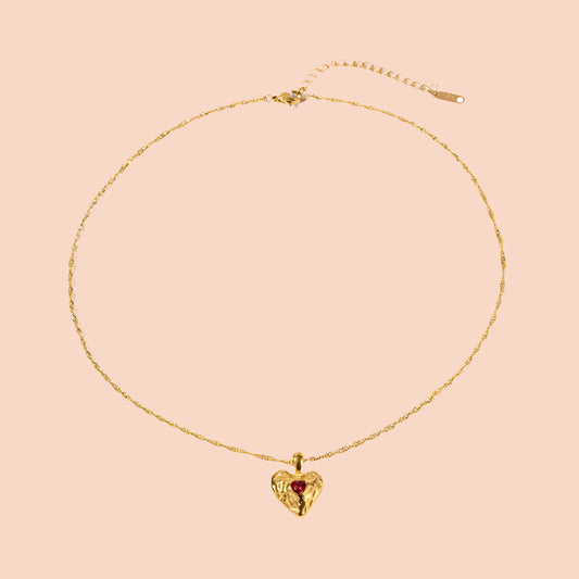 Gold necklace with a heart-shaped pendant on a pink background