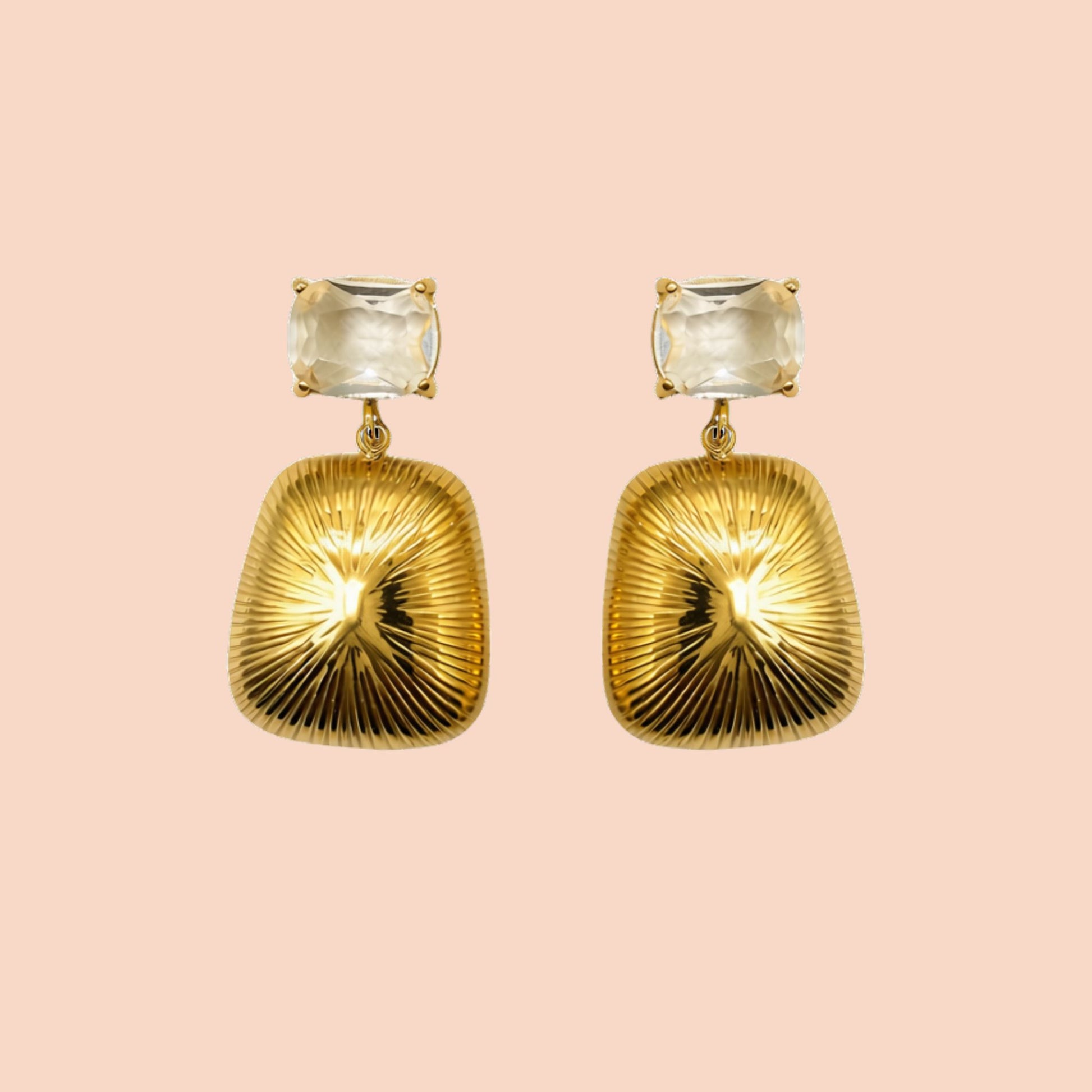 Gold earrings with clear gemstones on a pink background