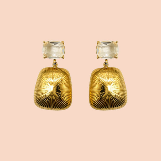 Gold earrings with clear gemstones on a pink background