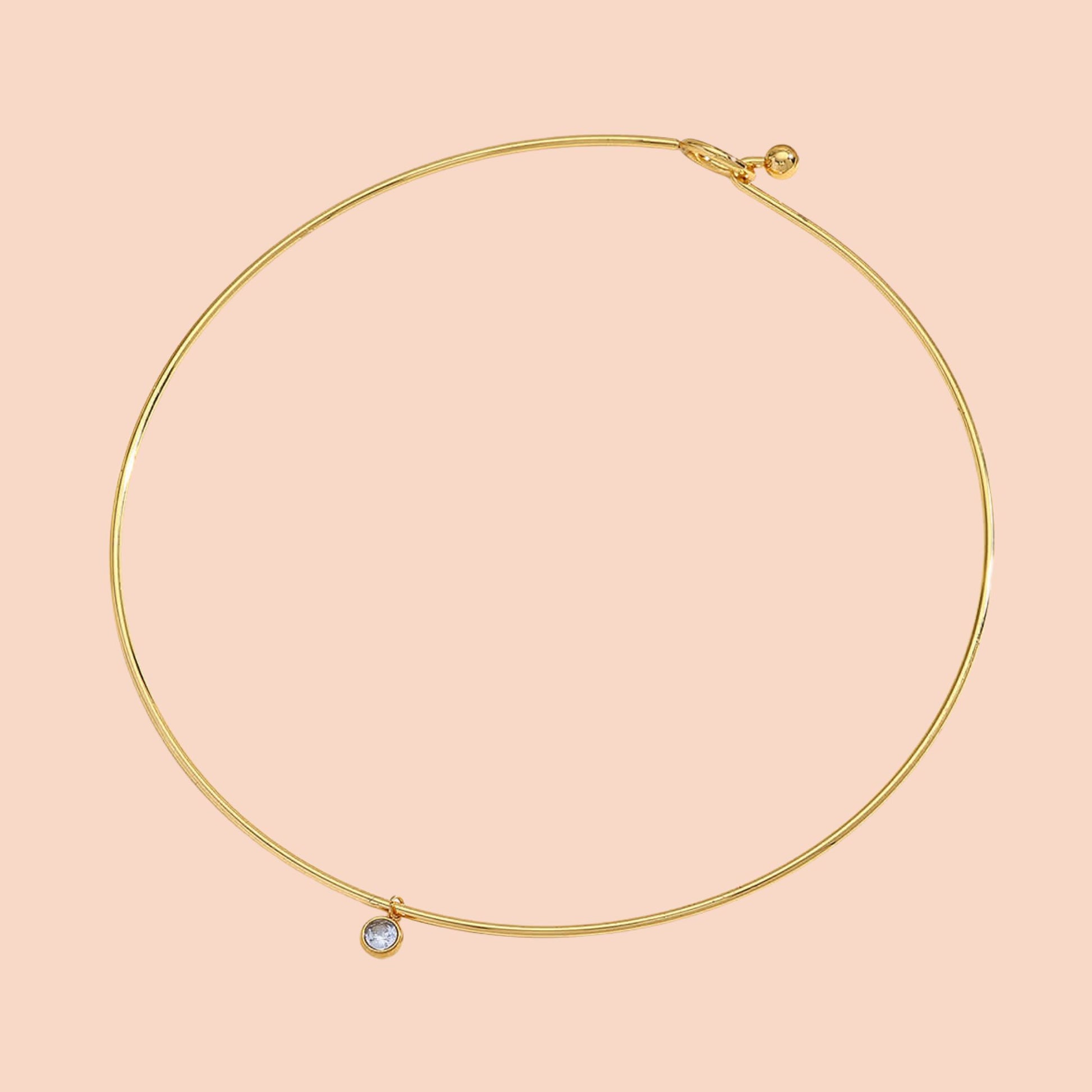 Gold necklace with a small gemstone on a pink background