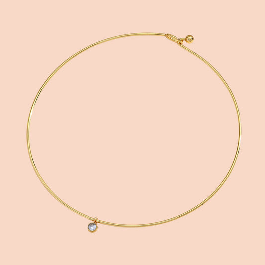 Gold necklace with a small gemstone on a pink background