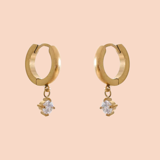 Gold hoop earrings with small diamond-like stones on a peach background