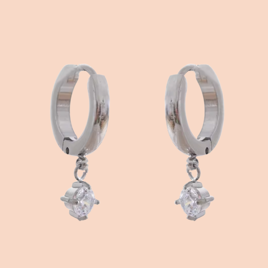 Silver hoop earrings with small diamond-like stones on a peach background