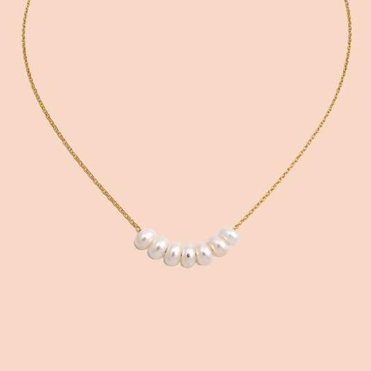 Pearl necklace on a gold chain against a pink background