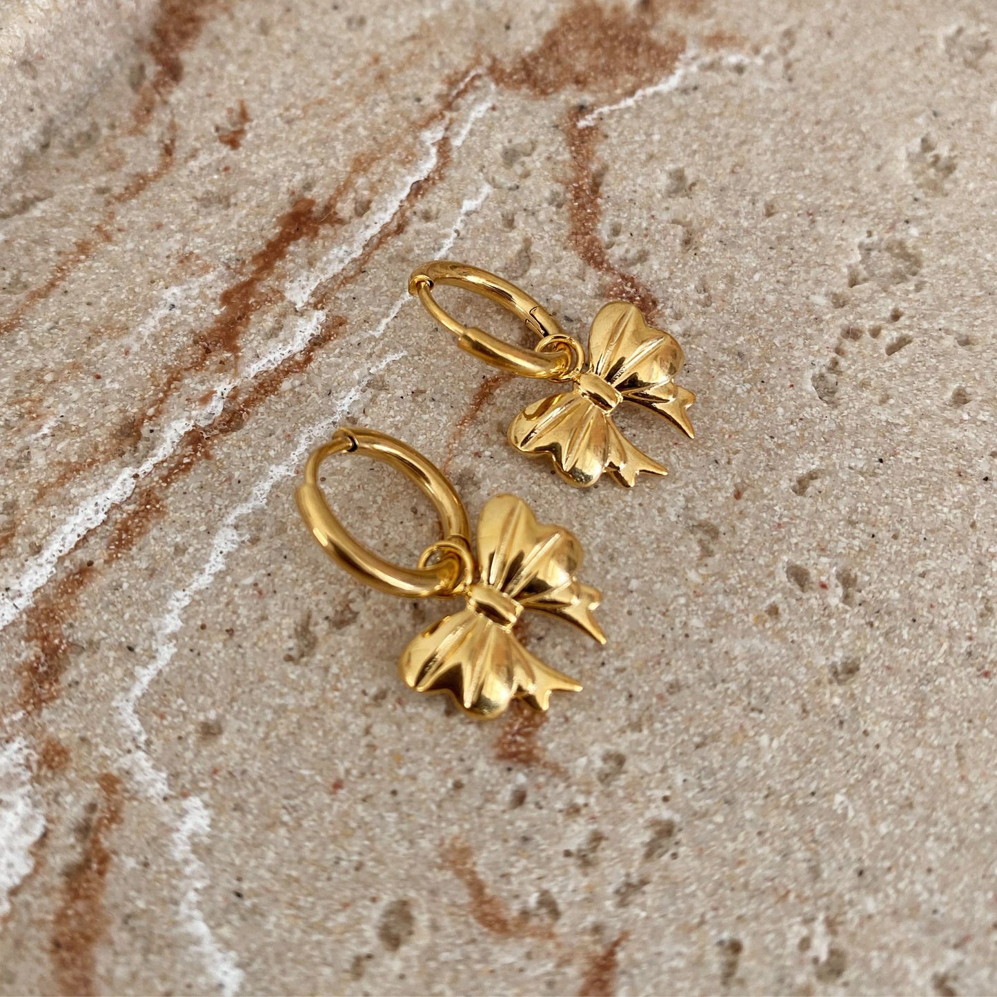 Gold bow-shaped earrings on a textured beige surface