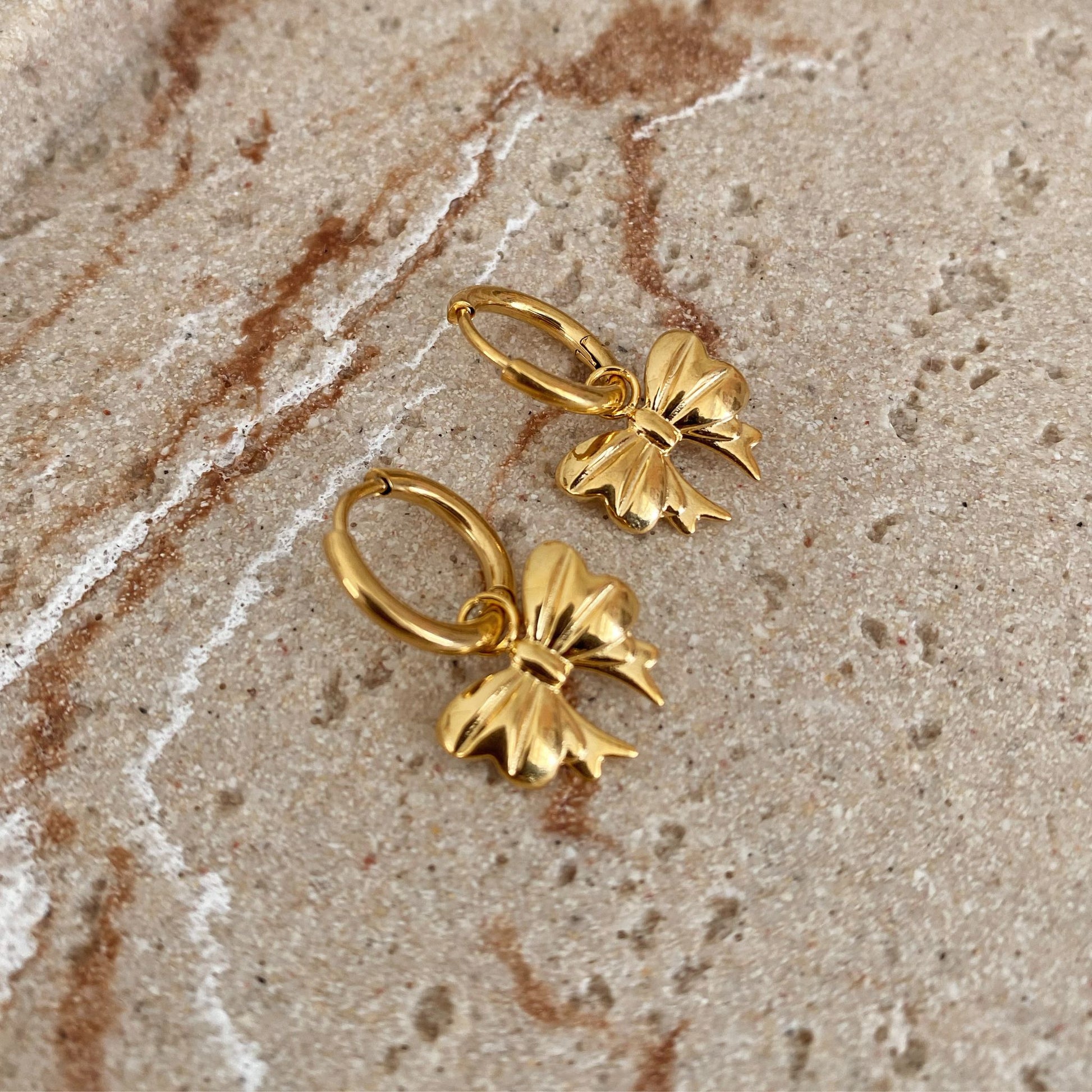 Gold bow-shaped earrings on a textured beige surface