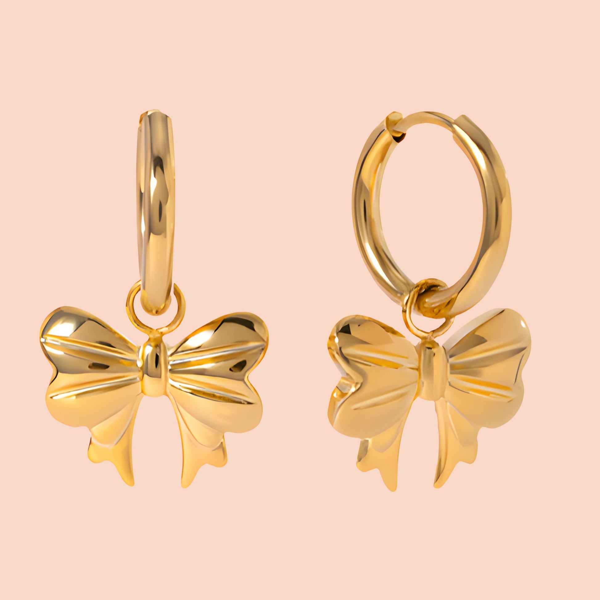 Gold bow-shaped earrings on a light pink background