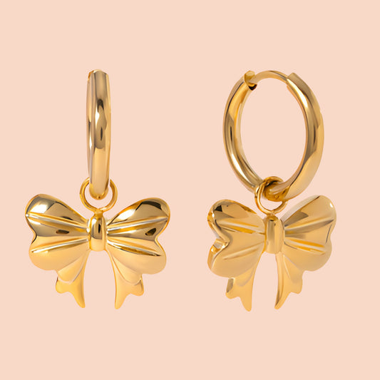 Gold bow-shaped earrings on a light pink background