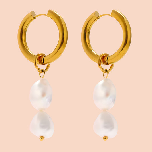 Gold hoop earrings with pearl drops on a peach background