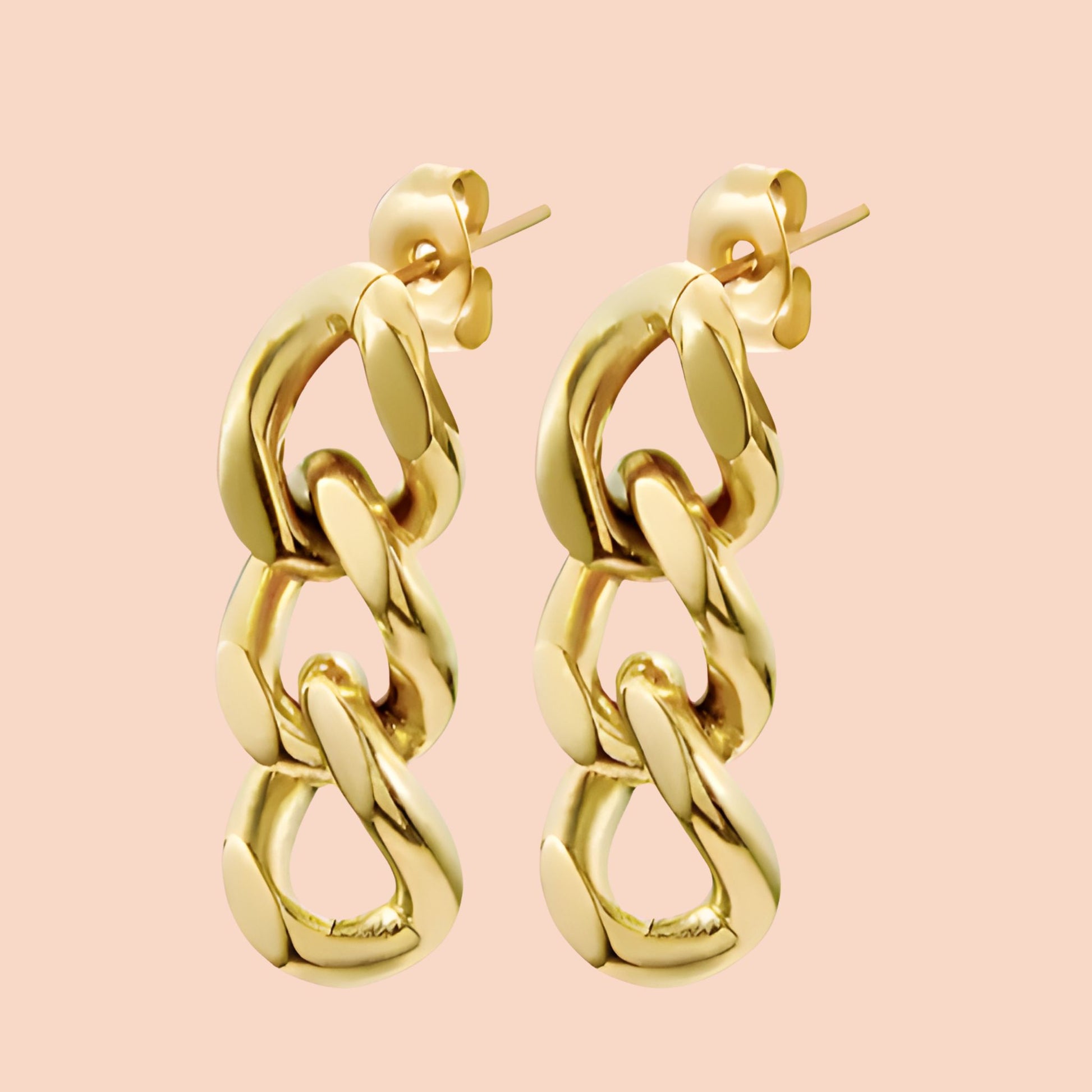 Gold chain-style earrings on a pink background
