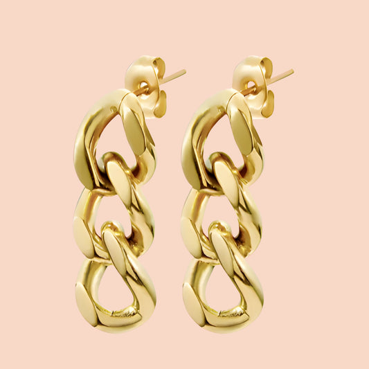 Gold chain-style earrings on a pink background