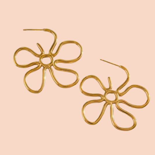 Gold flower-shaped earrings on a pink background