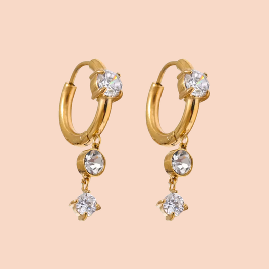 Gold hoop earrings with crystal drops on a beige background