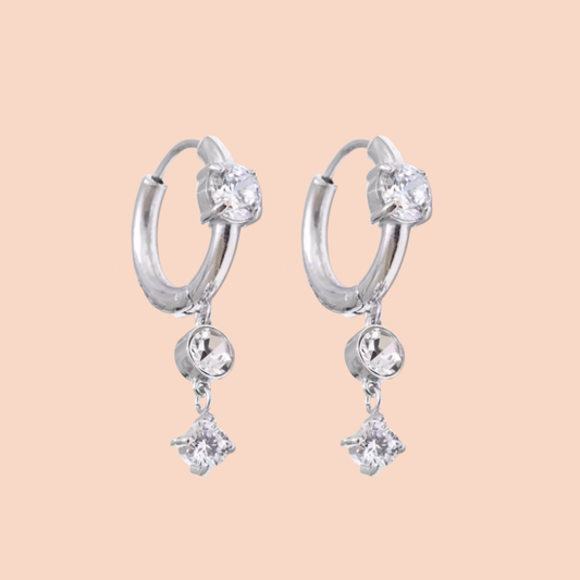 Silver hoop earrings with clear gemstones on a beige background