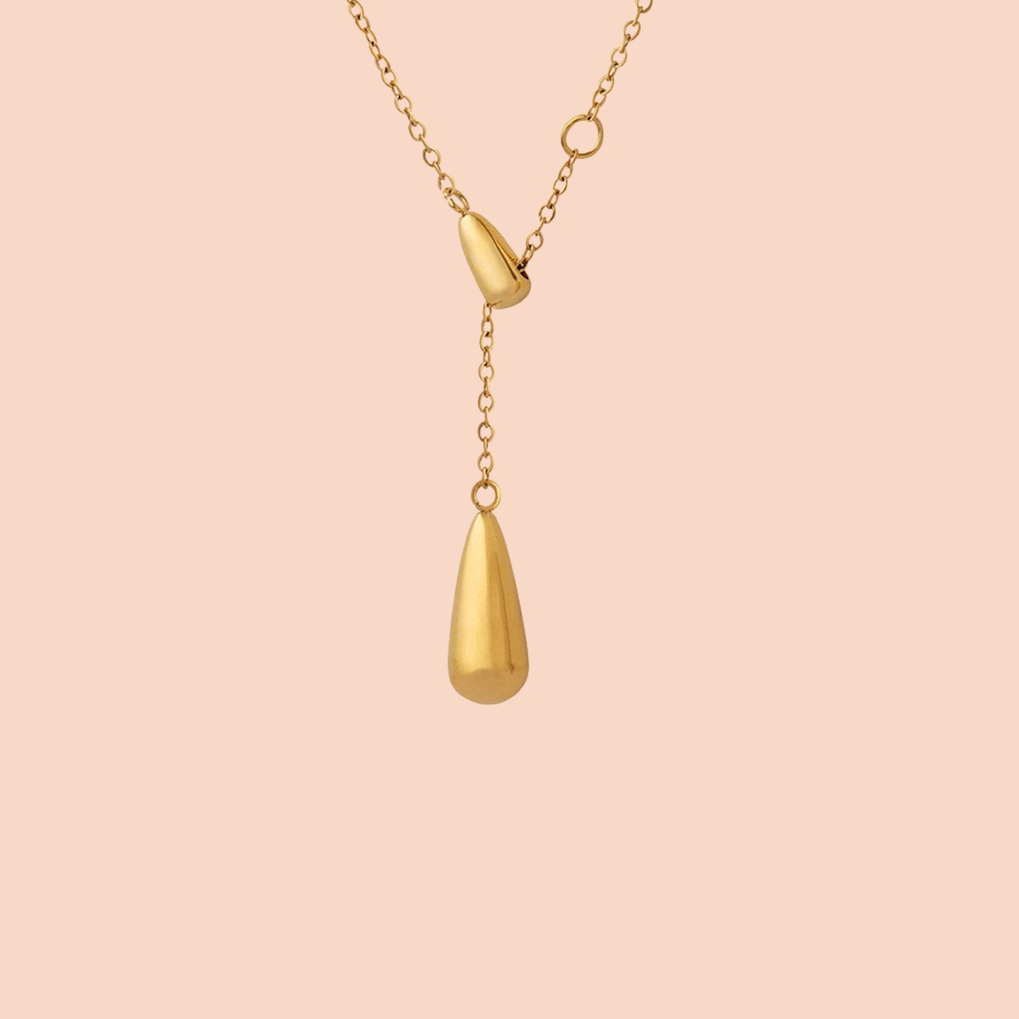 Gold necklace with a teardrop pendant on a pink background