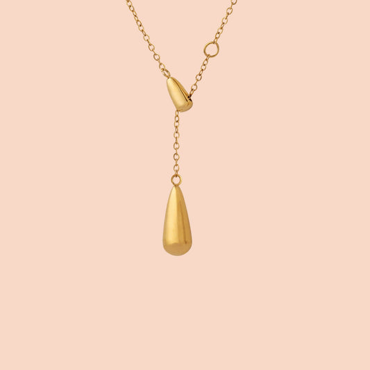 Gold necklace with a teardrop pendant on a pink background