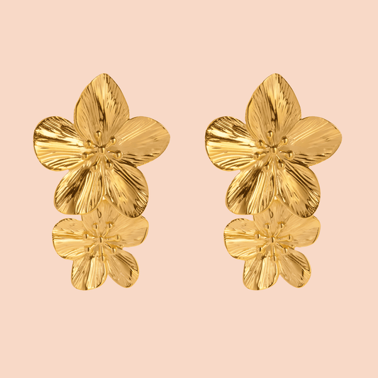 Gold floral earrings on a pink background