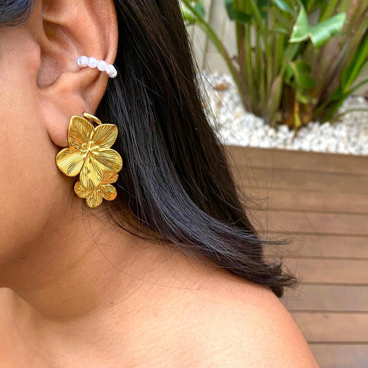 Close-up of a person wearing a gold floral earring with a blurred outdoor background.