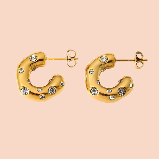 Gold hoop earrings with embedded crystals on a beige background
