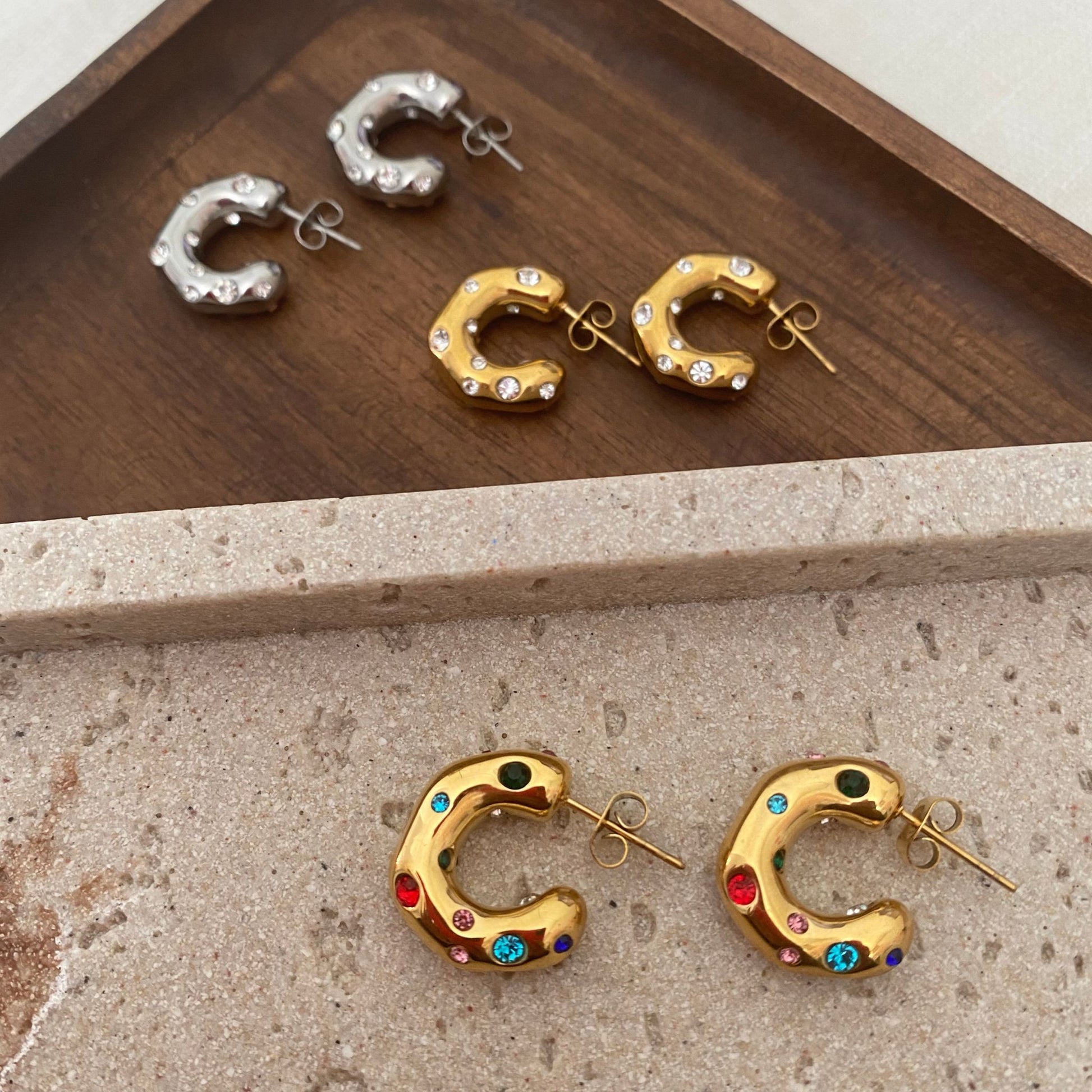 Gold hoop earrings with colorful gemstones on a stone surface
