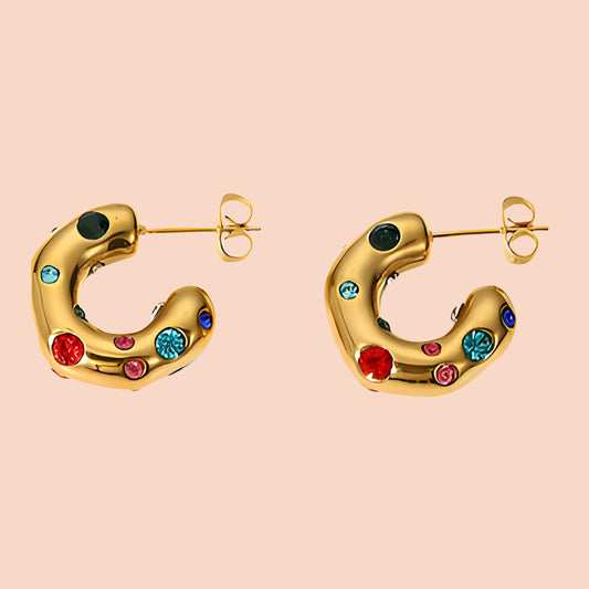 Gold hoop earrings with colorful gemstones on a beige background