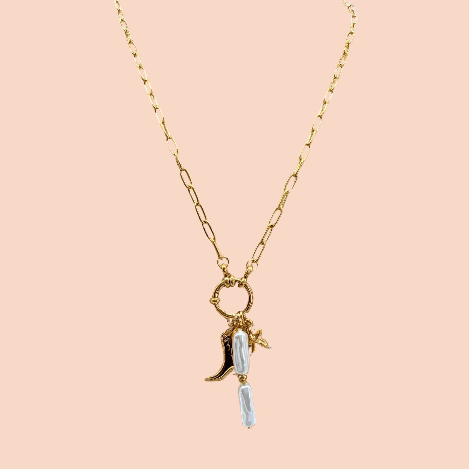 Gold necklace with a boot and star charm on a pink background