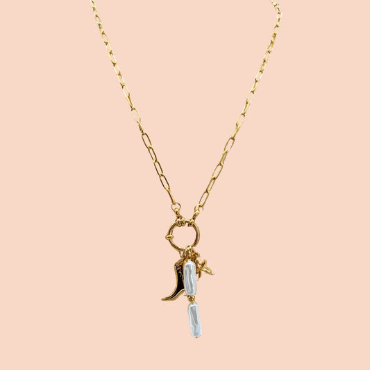 Gold necklace with a boot and star charm on a pink background