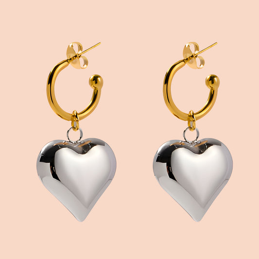 Gold hoop earrings with silver heart pendants on a beige background