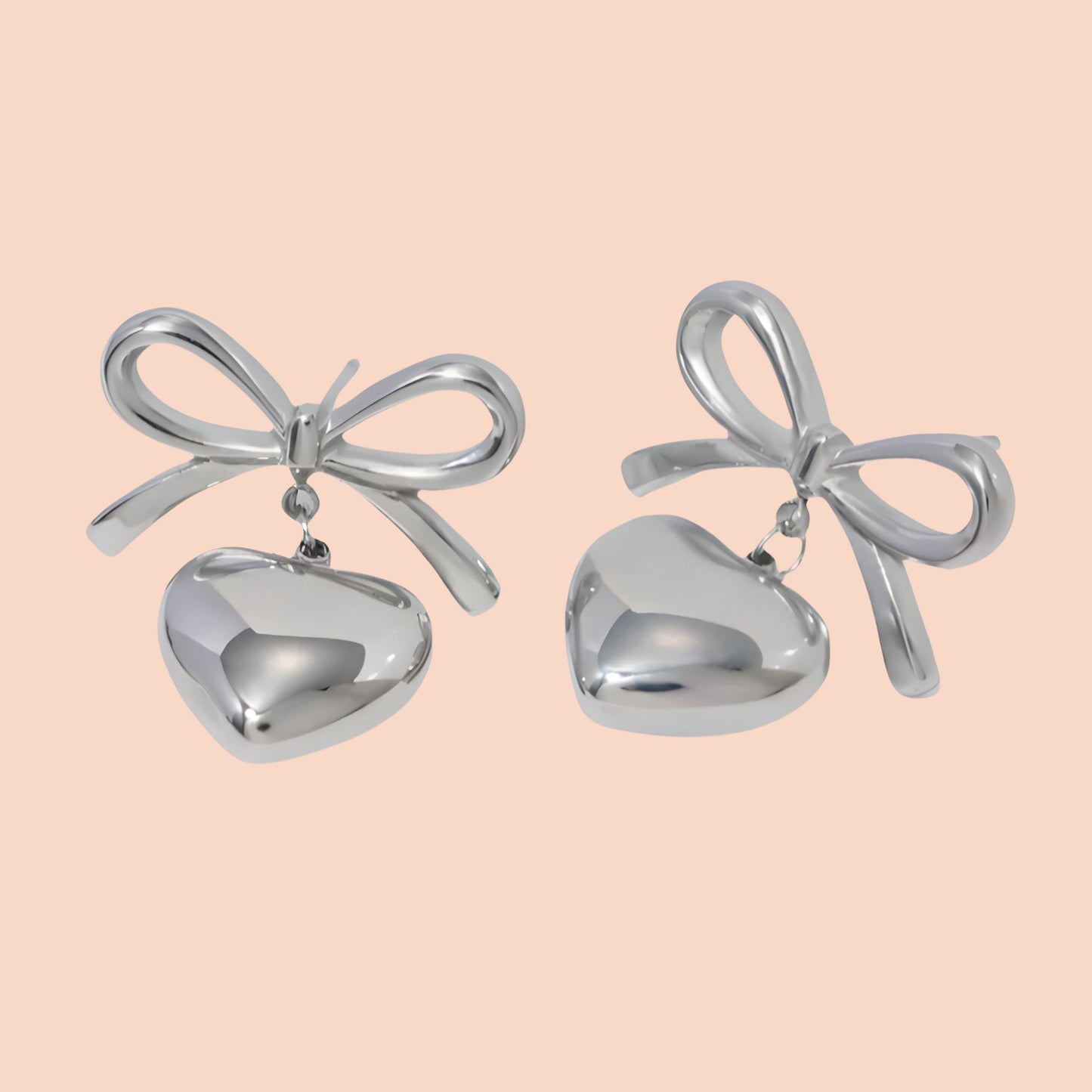 Silver bow-shaped earrings with heart details on a light pink background