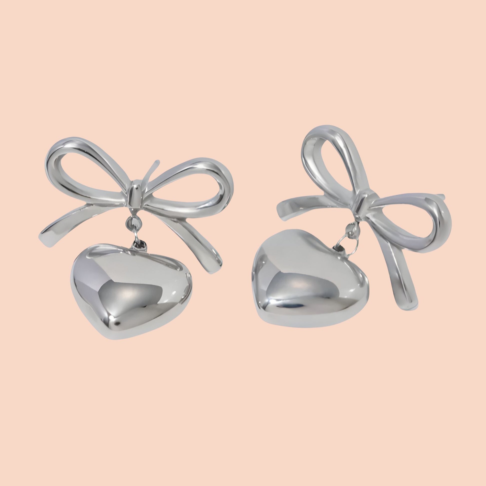 Silver bow-shaped earrings with heart details on a light pink background