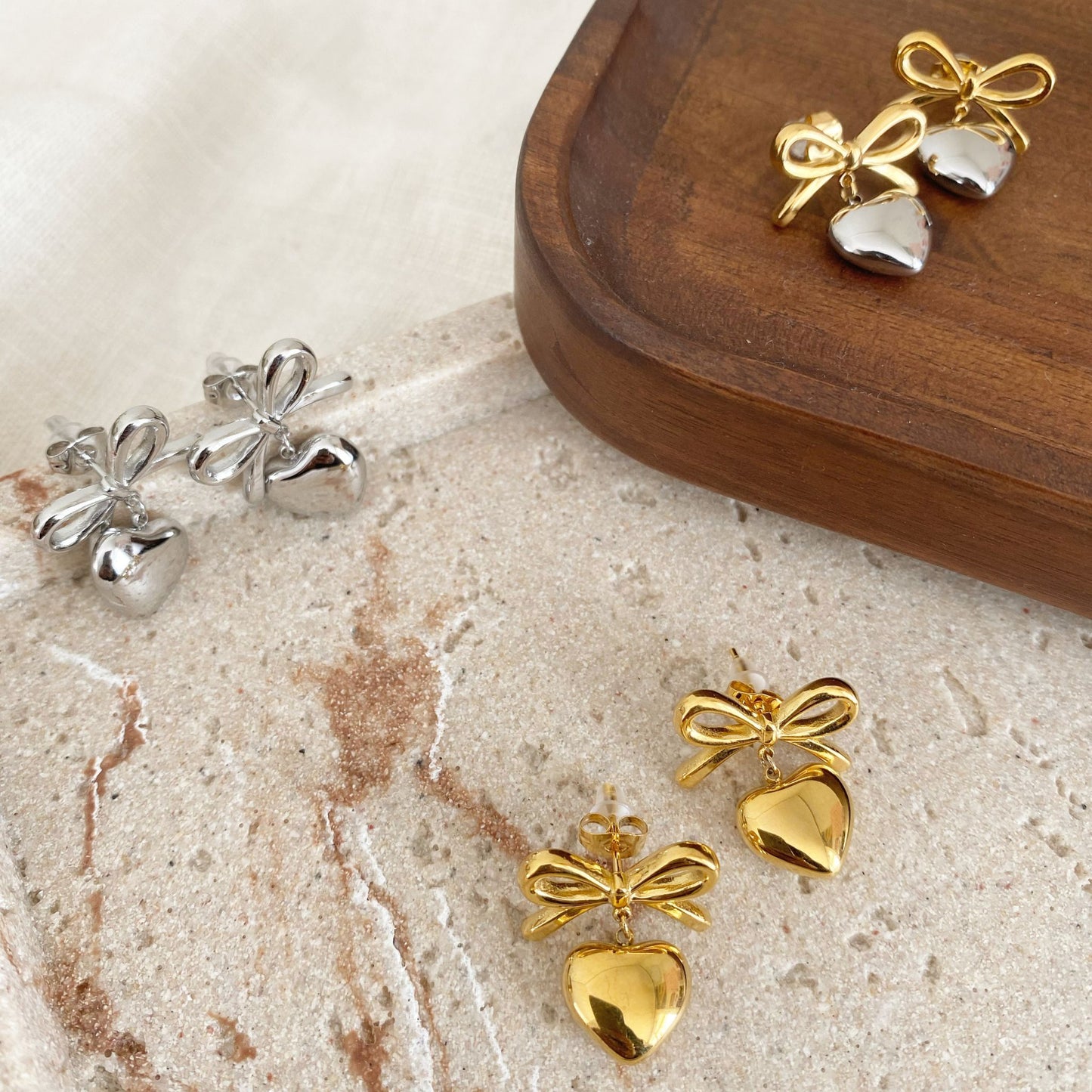 Gold and silver bow-shaped earrings on a marble surface with a wooden box.