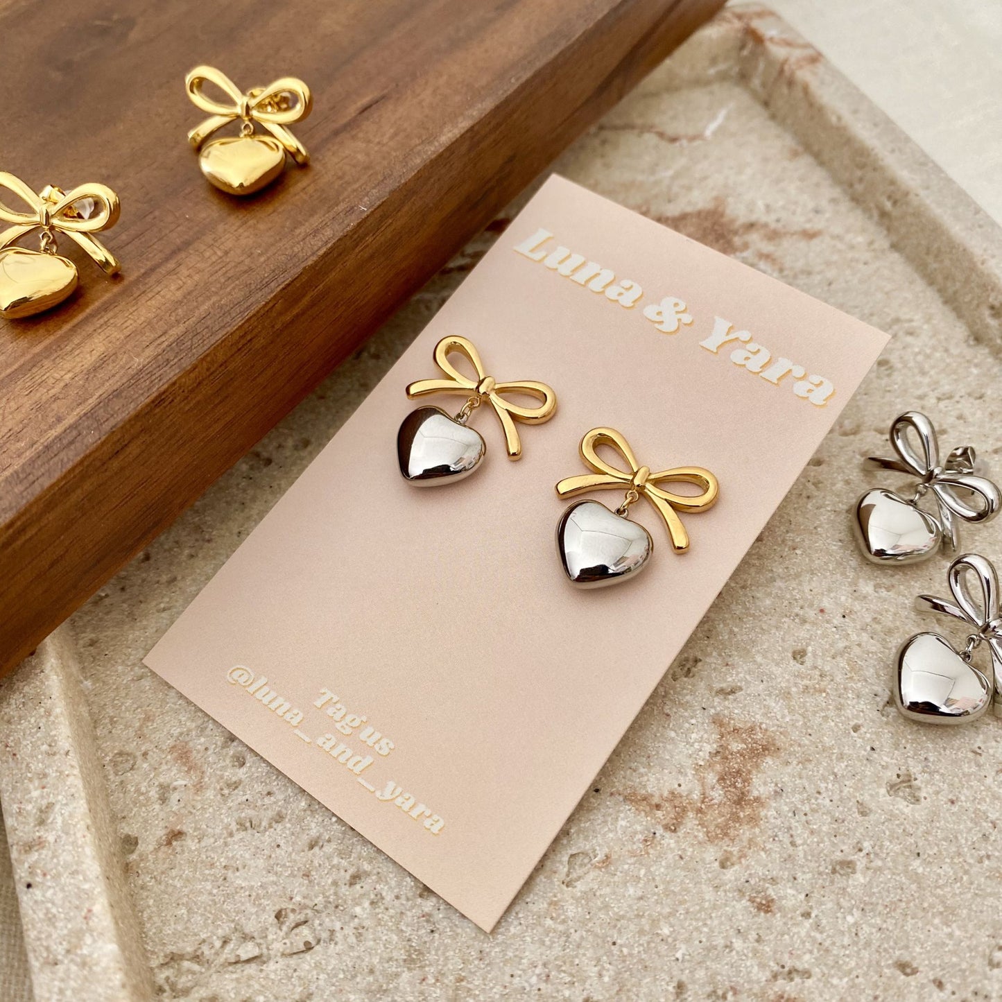 Gold and silver bow-shaped earrings on a Luna & Yara card with a wooden box in the background.