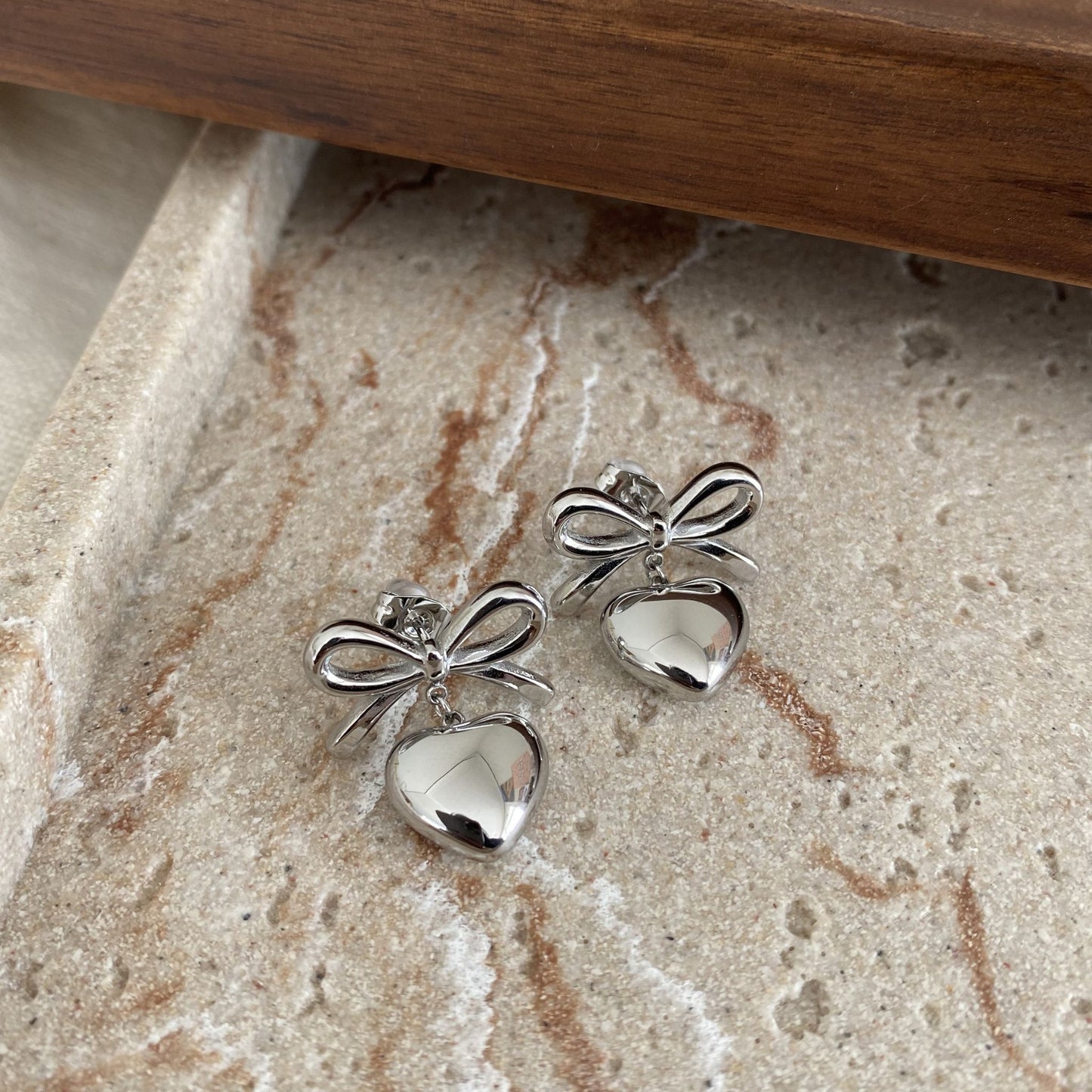 Silver bow-shaped earrings on a textured stone surface