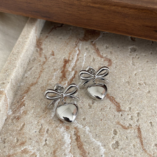 Silver bow-shaped earrings on a textured stone surface