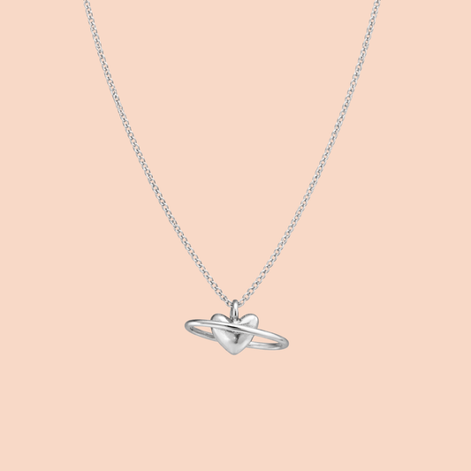 Silver necklace with a heart-shaped pendant on a light pink background
