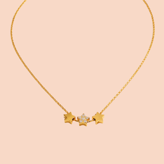 Gold necklace with star-shaped pendants on a peach background